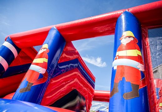 Inflatable covered bounce house in the theme of a fire department with a slide on the jumping surface, climbing tower and fun obstacles for kids. Buy bounce houses online at JB Inflatables UK